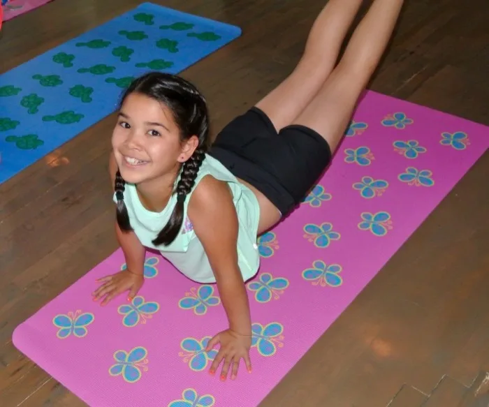 Girl posing in a yoga stretch on a butterfly-print mat at a birthday party