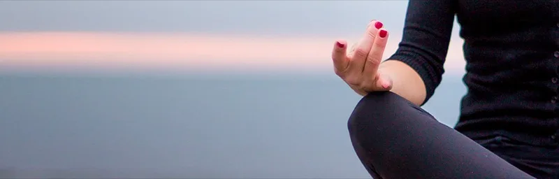 Close up of a hand in meditation mudra against the ocean at dusk